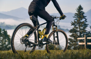 Osoba na rowerze górskim zjeżdżająca ze stromej ścieżki na tle zachodzącego słońca i majestatycznych górskich szczytów.
