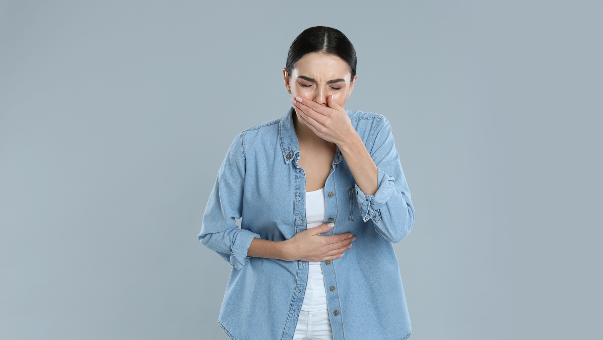 Grypa żołądkowa powoduje bóle brzucha i wymioty co pokazuje kobieta trzymająca się za brzuch i twarz